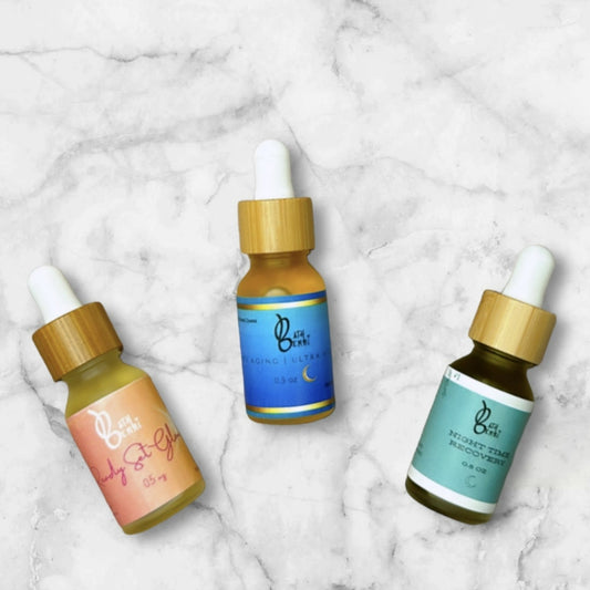 Three small dropper bottles of luxury face oil placed on a marble surface. Each bottle has a different color label, indicating different variants of the oil.