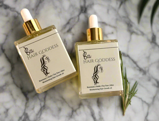 Two glass bottles of hair growth oil with a rosemary leaf on a marble background