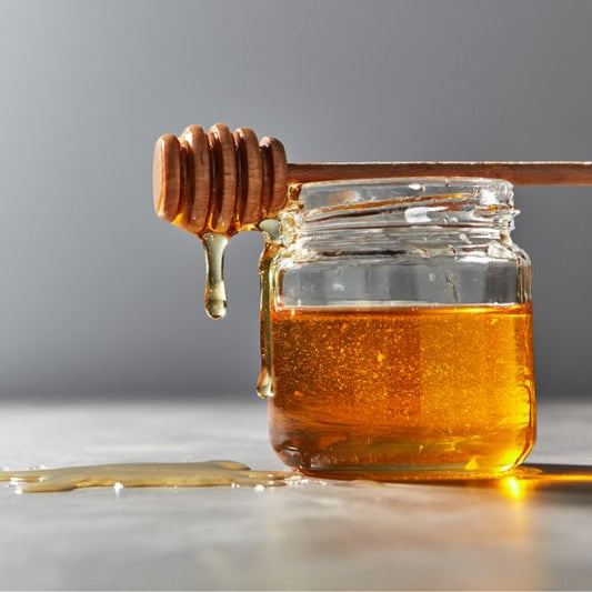 Jar of honey with a wooden dipper on a gray background