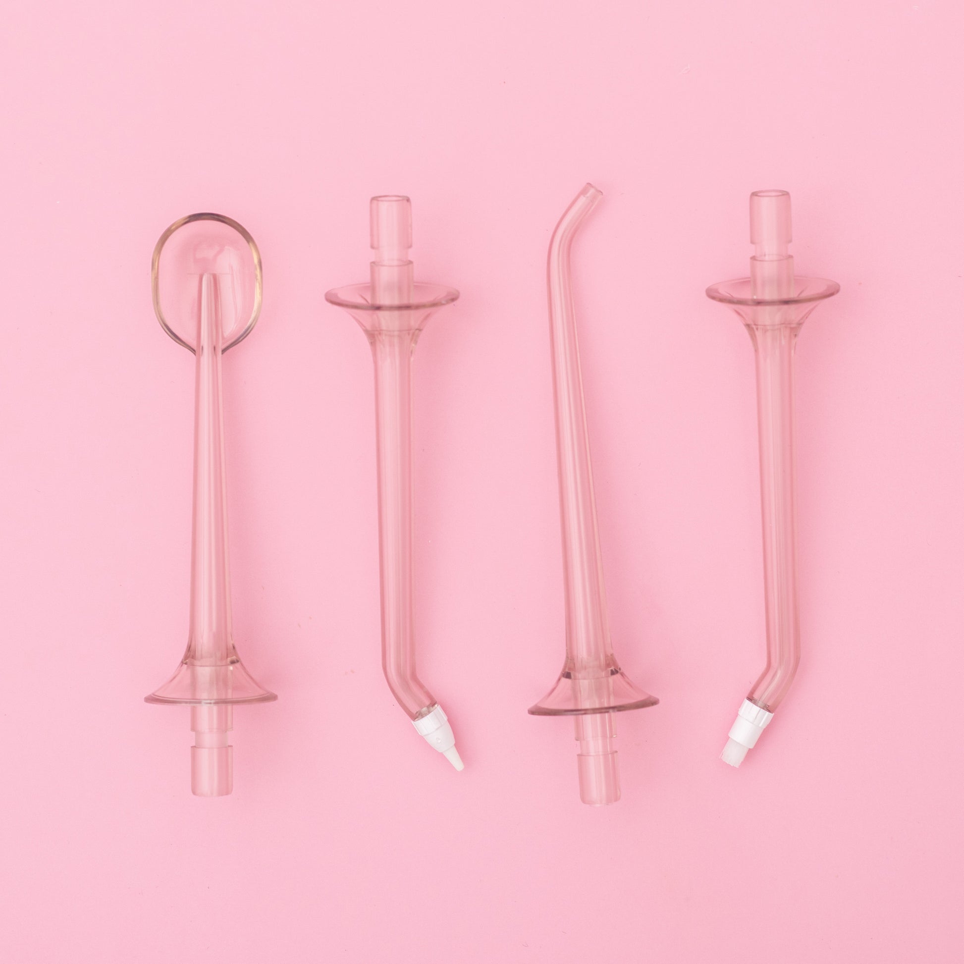 Set of four pink glass dental straws on a pink background