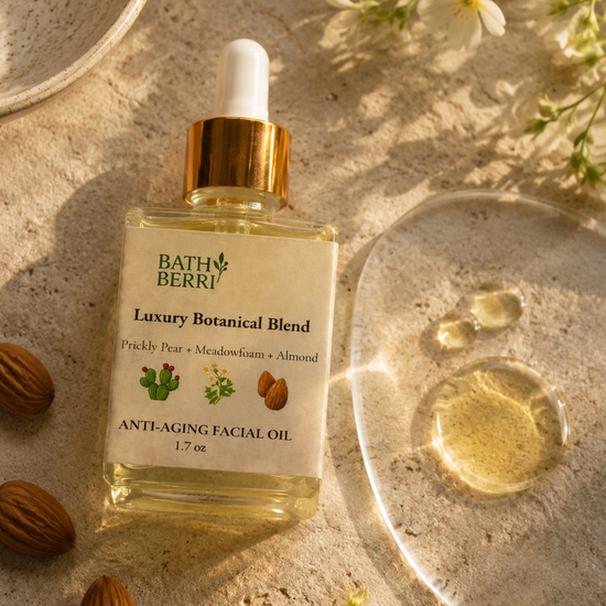 Bath Berri Luxury Botanical Blend Anti-Aging Facial Oil in a clear dropper bottle with a gold collar, styled on a sandy surface with almonds, white flowers, and a glass dish showing the golden oil.