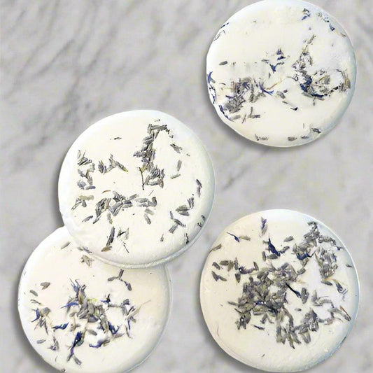 Four round shower steamers infused with essential oils, displayed on a marble surface.