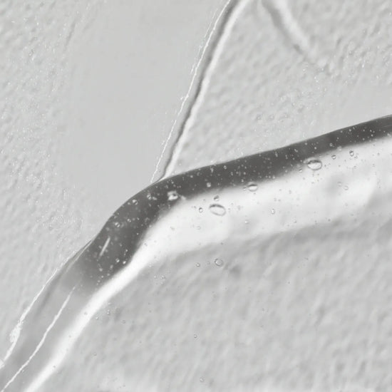 Close-up of a droplet on a reflective surface with a light gray background