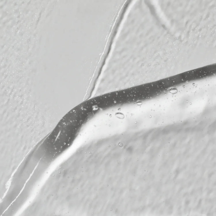 Close-up of a droplet on a reflective surface with a light gray background