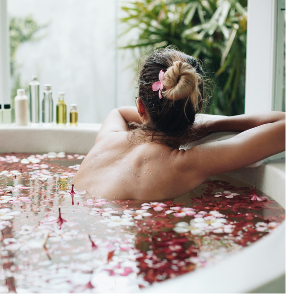 Woman relaxing in a bathtub filled with rose petals, surrounded by greenery.