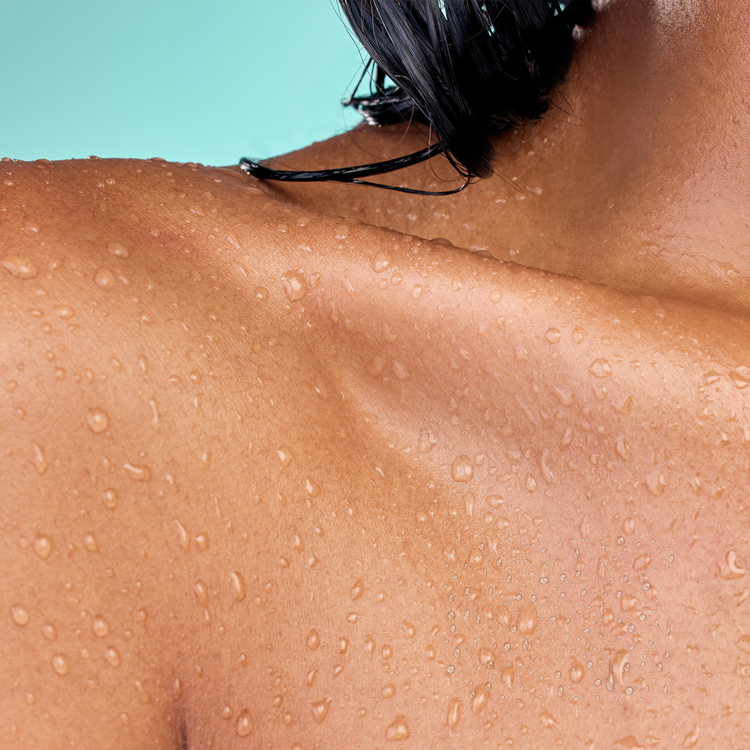 Close-up of a person's shoulder with water droplets on a light blue background